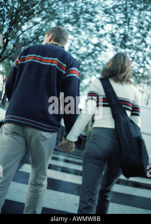 Coppia giovane holding hands attraversando sulle strisce pedonali, vista posteriore Foto Stock