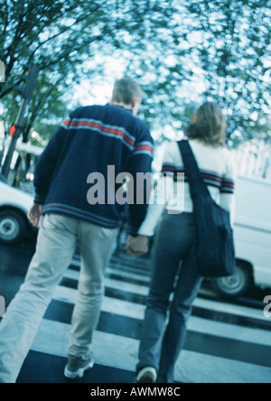 Coppia giovane Holding Hands, incrocio con attraversamento pedonale, offuscata, vista posteriore Foto Stock