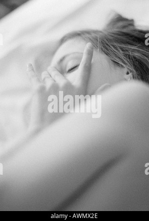 Donna sdraiata sul letto, toccando il viso, close-up, in bianco e nero Foto Stock