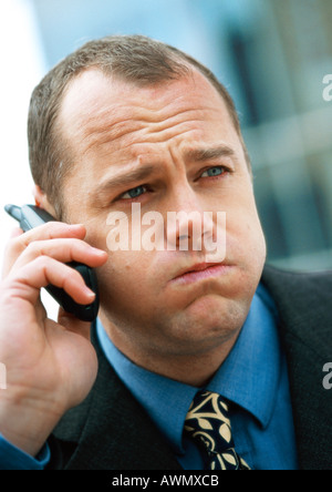 Imprenditore tramite telefono cellulare, sbuffando fuori le guance e solcano brow, ritratto, close-up. Foto Stock