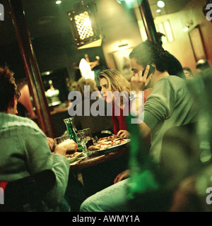 Un gruppo di giovani di mangiare al tavolo nel ristorante, un uomo tramite telefono cellulare. Foto Stock