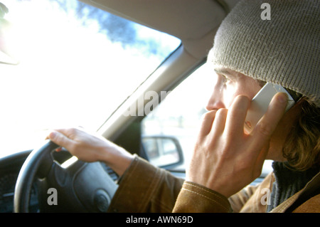 Giovane uomo illegalmente auto di guida mentre si parla al telefono cellulare, England, Regno Unito Foto Stock