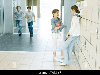 Due ragazze adolescenti parlando di armadietti mentre i ragazzi corrono attraverso il corridoio Foto Stock