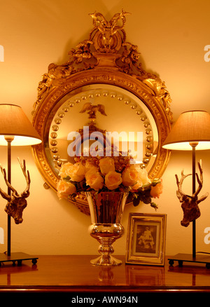 Fiori artificiali in un vaso posto nella parte anteriore di un oro-specchio incorniciato Foto Stock