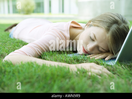 Teen ragazza dorme con la testa sul laptop, giacente in erba Foto Stock