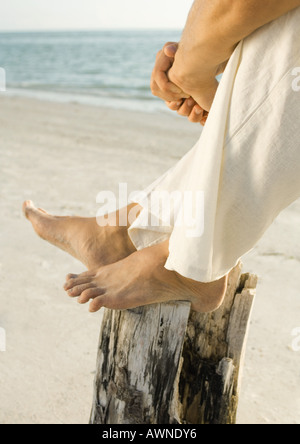 Uomo seduto sulla spiaggia con i piedi sul palo di legno, sezione bassa Foto Stock