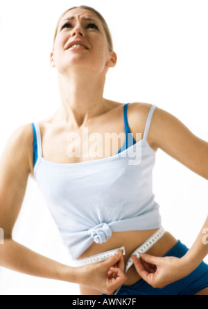 Donna che guarda verso l'alto, misurando in vita con nastro di misurazione, basso angolo di visione Foto Stock