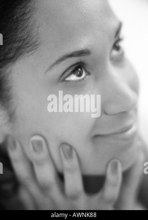 Donna che mantiene il viso con le mani, guardando in alto, close-up, B&W. Foto Stock