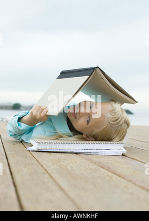 Ragazza distesa sul dock con libro sopra la testa Foto Stock