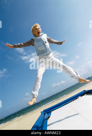 Donna matura di saltare sul trampolino presso la spiaggia, braccia, gambe diffusione Foto Stock