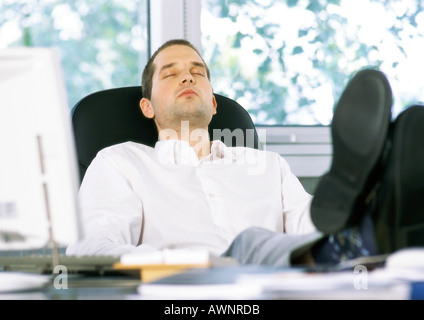 Imprenditore seduto con i piedi sulla scrivania e gli occhi chiusi Foto Stock