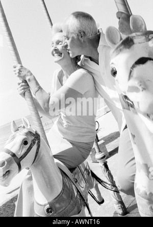 Uomo maturo kissing donna matura sulla guancia su una giostra, B&W Foto Stock