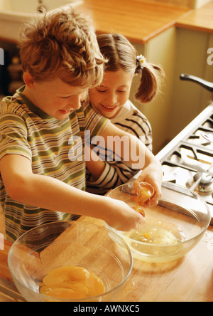 Due bambini sorridenti in cucina con una ciotola di tuorli e una ciotola di albumi montati a neve Foto Stock