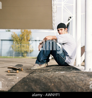 Giovane uomo con lo skateboard seduti all'aperto, vista laterale, ritratto Foto Stock