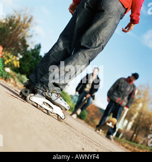 I giovani su indossando pattini a rotelle in linea, altri con skateboard, sezione bassa Foto Stock