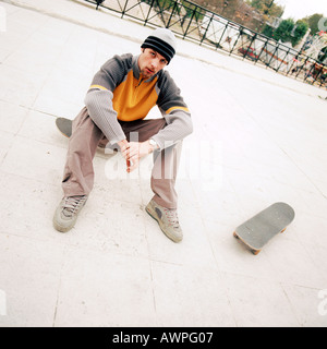 Giovane uomo seduto su skateboard Foto Stock