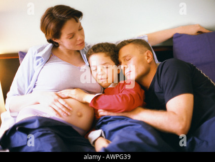 Donna incinta seduta con uomo e bambino nel letto Foto Stock