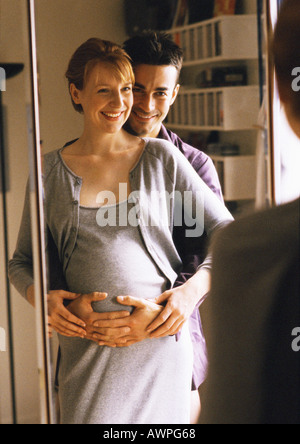 Uomo in piedi con le braccia intorno a donna incinta nella parte anteriore dello specchio Foto Stock