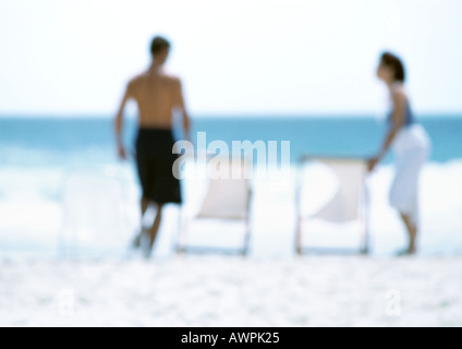 Due adulti in piedi accanto a sedie a sdraio sulla spiaggia, sfocato Foto Stock