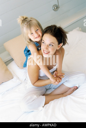 Madre seduta sul letto, tenendo ragazza sul retro Foto Stock