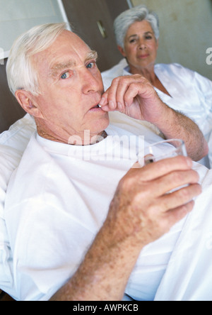 Coppia senior in letto, l'uomo prendendo pillola Foto Stock