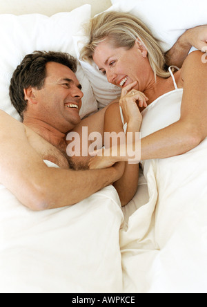 Coppia giacendo in letto a sorridere e ridere Foto Stock