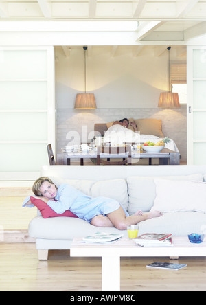 Donna sdraiati sul divano, uomo disteso nel letto in background Foto Stock