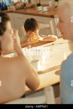 Bambini al tavolo a bere dal bicchiere, con due donne Foto Stock