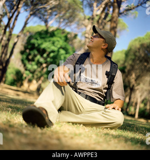 Uomo seduto su erba in foresta, guardando in alto Foto Stock