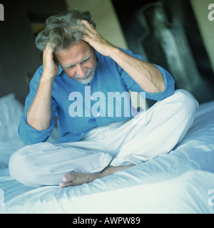 Uomo seduto in stile indiano sul letto, entrambe le mani nei capelli Foto Stock