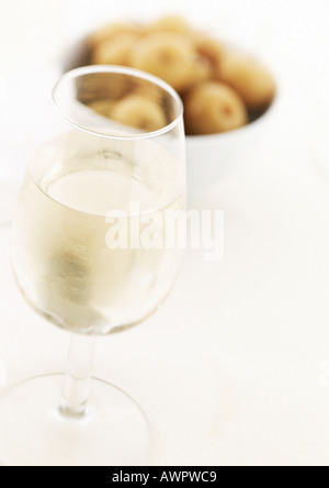 Bicchiere di vino bianco, ciotola di olive in background Foto Stock