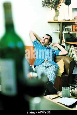 L uomo lo stiramento sul divano, una bottiglia di vino in primo piano Foto Stock