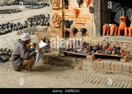 L'uomo leggendo un giornale davanti a un negozio di souvenir, Bhaktapur, Nepal Foto Stock