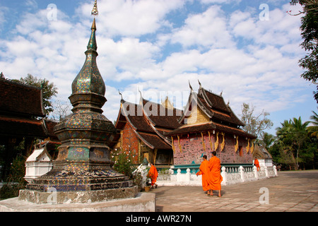 Laos Luang Prabang Wat Xieng Thong monaci oltrepassando stupa e sim Foto Stock