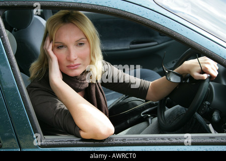 Donna bionda Sat in una vettura appoggiata sul volante e guardando fuori della finestra Foto Stock