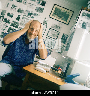 Senior uomo seduto al computer, le mani sulla testa Foto Stock