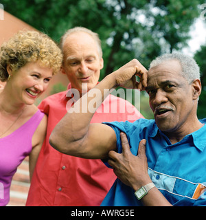 Tre persone in piedi fuori, uomo di flessione dei muscoli del braccio Foto Stock