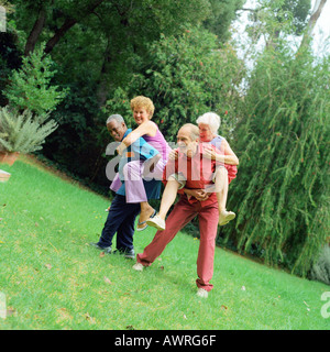 Due uomini maturi dando alle donne piggyback giostre, all'aperto Foto Stock