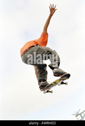 Giovane uomo su skateboard, saltando, mid-aria, angolo basso, in vista posteriore Foto Stock