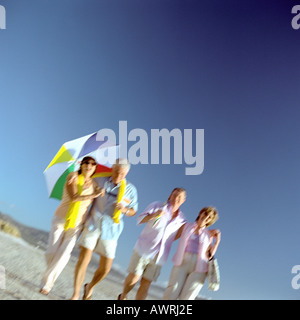 Due coppie mature camminando sulla spiaggia, donna ombrello di contenimento Foto Stock