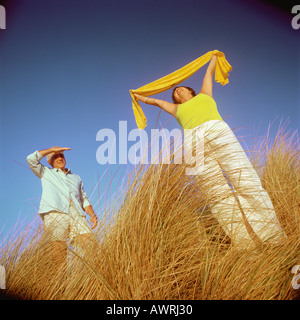 Coppia matura in piedi in erba alta, donna holding sciarpa sopra la testa Foto Stock