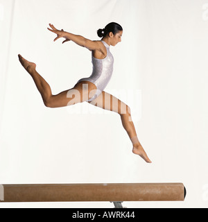 Giovani femmine ginnasta eseguendo sulla trave di equilibrio, mid-aria, vista laterale Foto Stock