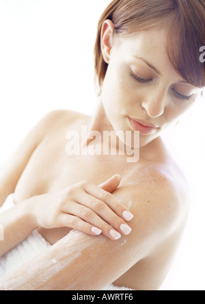 Giovane donna di applicare una crema idratante al braccio, close-up Foto Stock