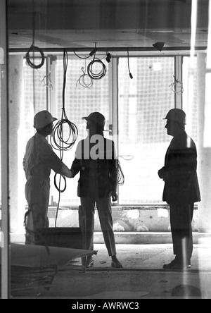 Tre persone con duro cappelli, due mani di scuotimento, b&W Foto Stock