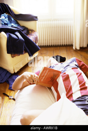 Uomo appoggiato sul letto con libro in mano Foto Stock