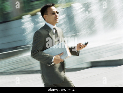 Imprenditore camminare con il cellulare in mano, tre quarti di lunghezza e inclinazione Foto Stock