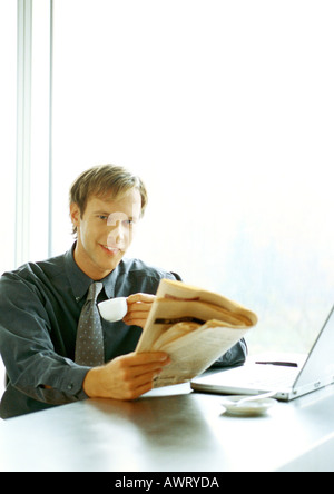 Imprenditore seduto alla scrivania, bere e la lettura Foto Stock