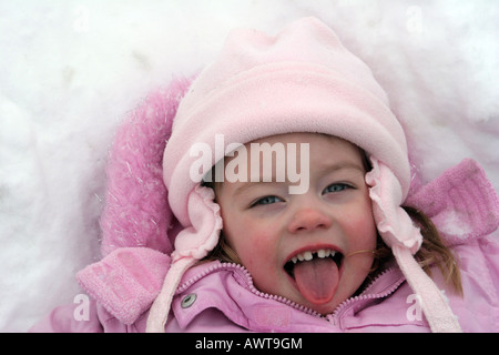 Una bambina di tre anni a giocare nella neve cercando di catturare i fiocchi di neve con la propria lingua Foto Stock