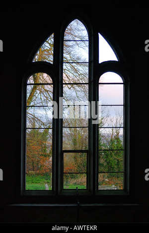 Vista attraverso un glassless finestra ad arco di una chiesa abbandonati bruciato da incendiari e lasciata come una rovina Foto Stock