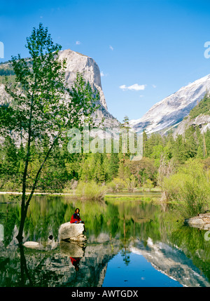 Parco Nazionale di Yosemite, Sierra Nevada, USA. Giovane donna escursionista si siede sulla roccia in Mirror Lake nel fiume Merced. Mezza Cupola dietro Foto Stock